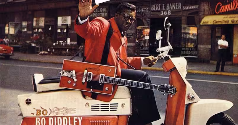 Bo Diddley sentado numa scooter com sua Cigar Box