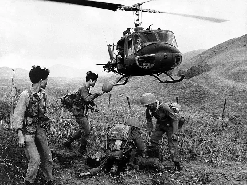 Uma foto em preto e branco de soldados na Guerra do Vietnã, carregando um companheiro ferido para um helicóptero.