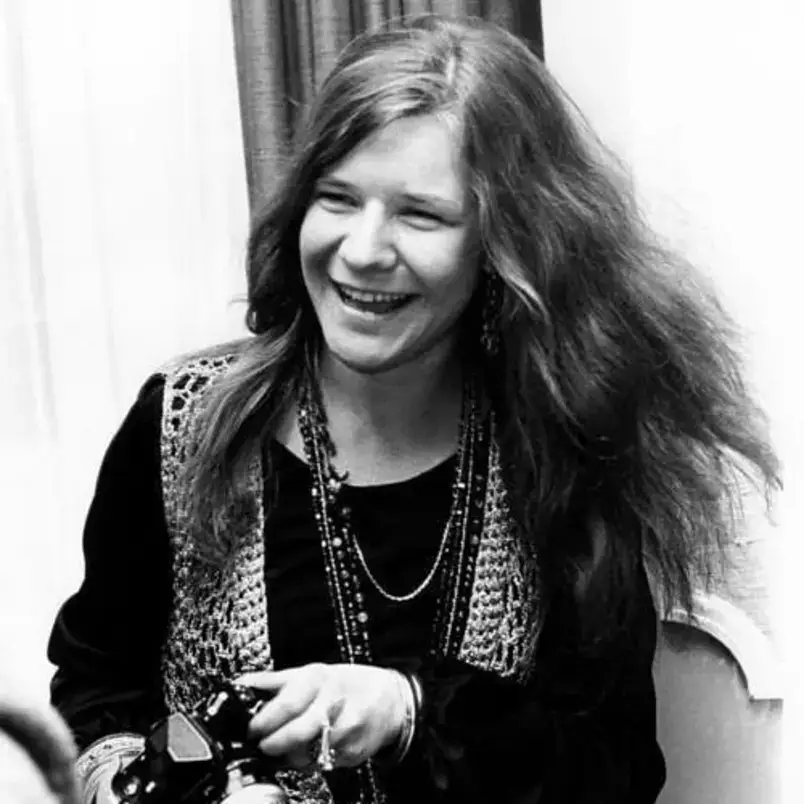 Uma foto em preto e branco de Janis Joplin, cantora de rock americana, sorrindo.