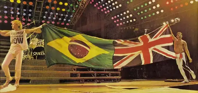 Membros do Queen segurando as bandeiras do Brasil e do Reino Unido em um show no Rock in Rio