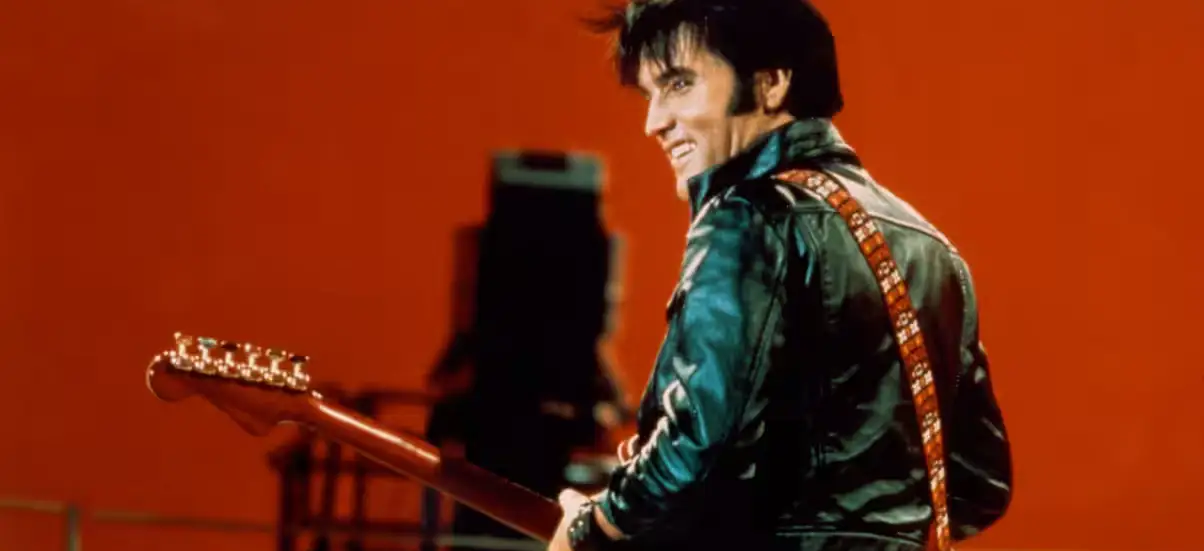 Elvis Presley de costas para a câmera, segurando uma guitarra durante o show de 1968