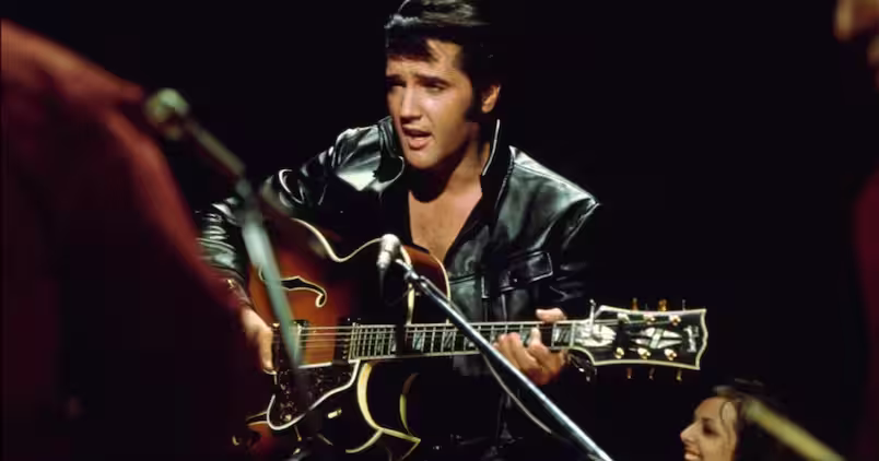 Elvis Presley sentado com uma guitarra semi acústica durante o show de 1968